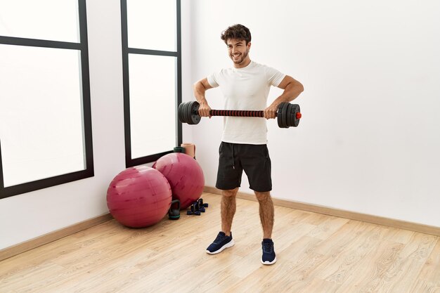 Young hispanic man smiling confident training with dumbbell at sport center