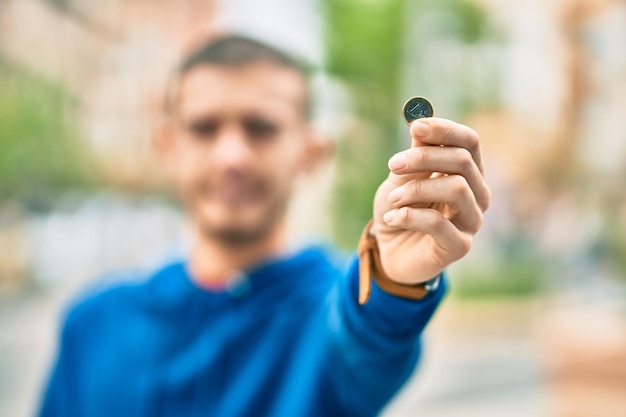 Foto gratuita giovane uomo ispanico che sorride felice tenendo una moneta da 1 euro in città