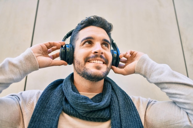 Free photo young hispanic man smiling happy listening to music using headphones at the city.