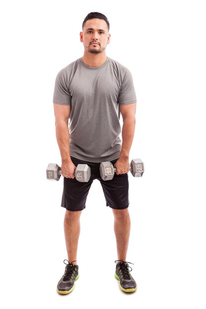 Young Hispanic man in sporty outfit raising dumbbells to strengthen his deltoids on a white background