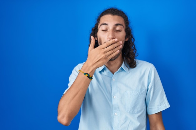 Free photo young hispanic man standing over blue background bored yawning tired covering mouth with hand restless and sleepiness