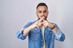 Free photo young hispanic man standing over isolated background rejection expression crossing fingers doing negative sign