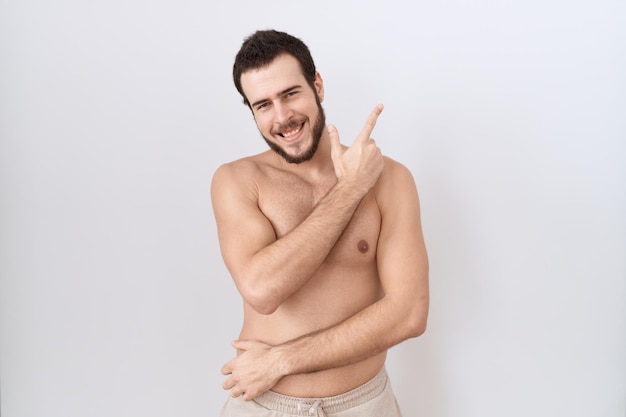 Free photo young hispanic man standing shirtless over white background cheerful with a smile of face pointing with hand and finger up to the side with happy and natural expression on face