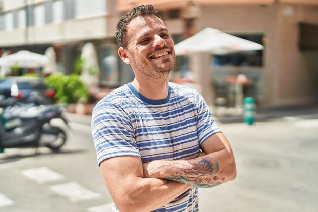 Young hispanic man standing with arms crossed gesture at street