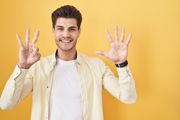Free photo young hispanic man standing over yellow background showing and pointing up with fingers number eight while smiling confident and happy.