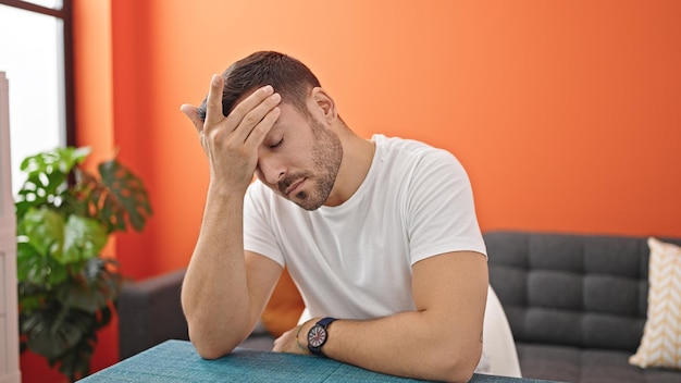 Free photo young hispanic man suffering for headache sitting on table at dinning room