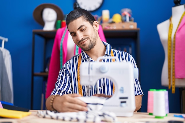 Бесплатное фото Молодой латиноамериканский портной уверенно улыбается, используя швейную машину в швейной студии