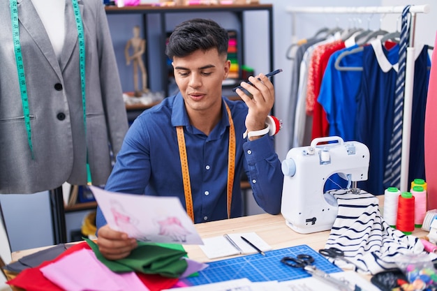Free photo young hispanic man tailor talking on smartphone looking clothing design at clothing factory