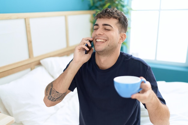 Giovane uomo ispanico che parla su smartphone bevendo caffè in camera da letto