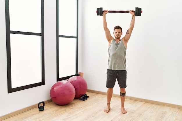 Young hispanic man training using dumbbells at sport center