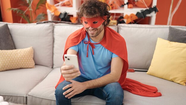 Young hispanic man using smartphone having halloween party at home