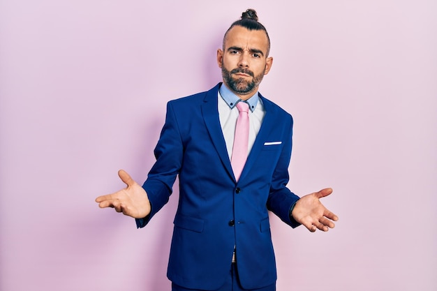 Free photo young hispanic man wearing business suit and tie clueless and confused with open arms, no idea concept.