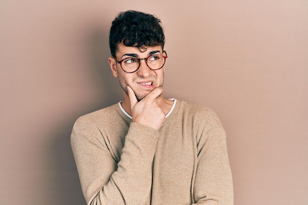Young hispanic man wearing casual clothes and glasses thinking worried about a question concerned and nervous with hand on chin