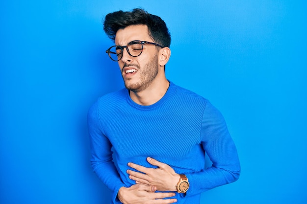 Free photo young hispanic man wearing casual clothes and glasses with hand on stomach because nausea painful disease feeling unwell ache concept