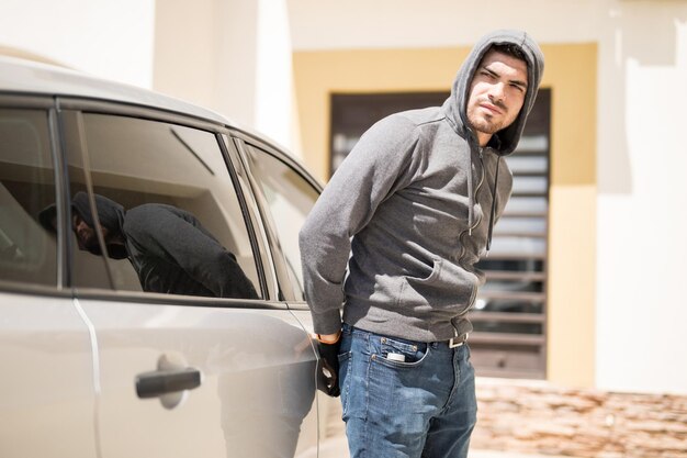 Young Hispanic man wearing a hoodie and trying to open a car door while no one watches