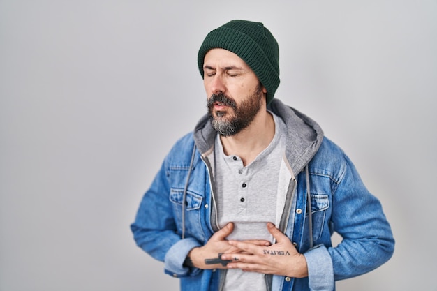 Free photo young hispanic man with tattoos wearing wool cap with hand on stomach because indigestion painful illness feeling unwell ache concept