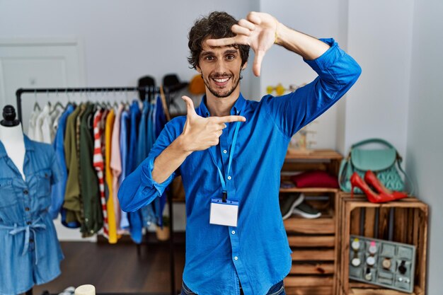 Young hispanic man working as manager at retail boutique smiling making frame with hands and fingers with happy face creativity and photography concept