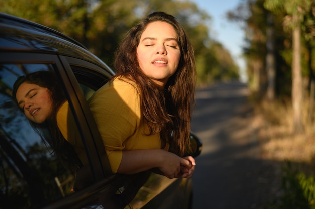 Young Hispanic woman enjoying sun out of car window on a bright day