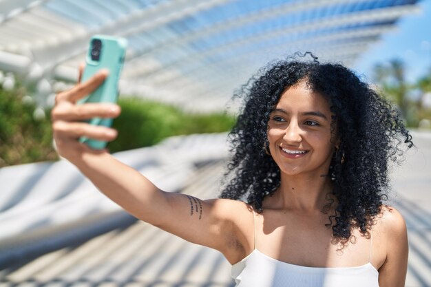 公園でスマートフォンで自分撮りをしながら自信を持って微笑む若いヒスパニック系女性