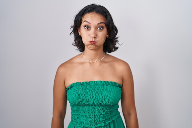 Free photo young hispanic woman standing over isolated background puffing cheeks with funny face mouth inflated with air crazy expression