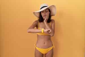 Free photo young hispanic woman wearing bikini and summer hat looking at the watch time worried afraid of getting late