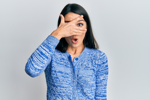 Young hispanic woman wearing casual clothes peeking in shock covering face and eyes with hand looking through fingers afraid