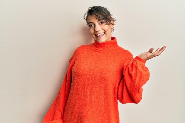 Young hispanic woman wearing casual winter sweater smiling cheerful presenting and pointing with palm of hand looking at the camera.