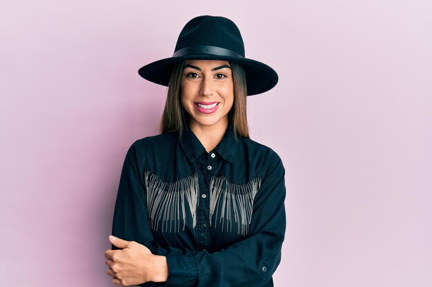 Young hispanic woman wearing cowgirl style happy face smiling with crossed arms looking at the camera. positive person.