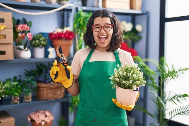Young hispanic woman working at florist shop celebrating crazy and amazed for success with open eyes screaming excited
