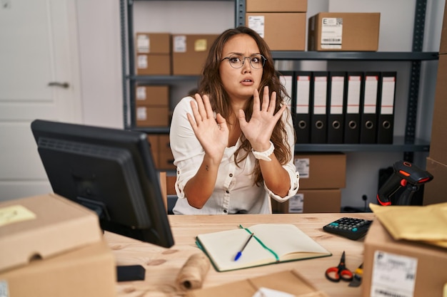 Young hispanic woman working at small business ecommerce moving away hands palms showing refusal and denial with afraid and disgusting expression stop and forbidden