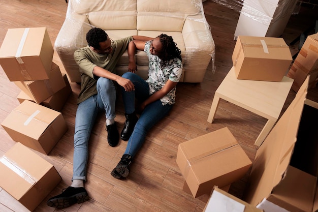 Free photo young homeowners enjoying new household property, taking break on floor after moving in together. relaxing on moving day, buying first apartment home on mortgage loan. top view of.