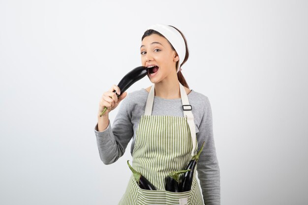 Young housewife eating fresh eggplant on white 