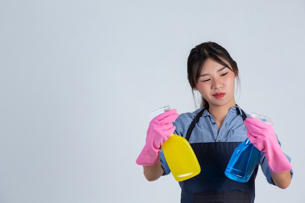 Young housewife is wearing yellow gloves while cleaning with the product of clean on white wall.