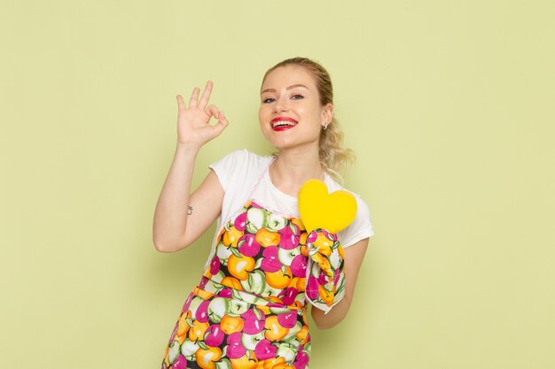 young housewife in shirt and colored cape holding yellow heart shape smiling on green