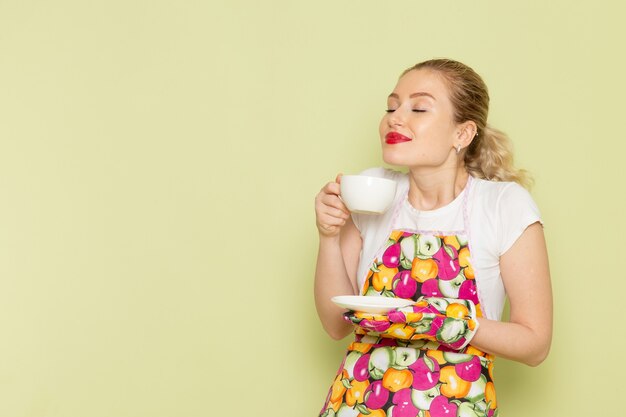 緑のお茶のカップでポーズのシャツと色のケープの若い主婦