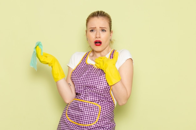 young housewife in shirt and colored cape wearing yellow gloves confused on green