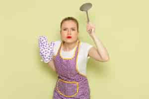 Free photo young housewife in shirt and purple cape gloves threatens with spoon on green