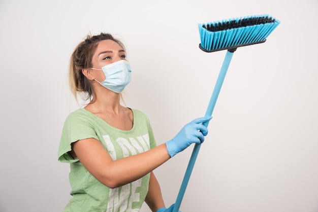 Free photo young housewife with facemask looking at broom on white wall.