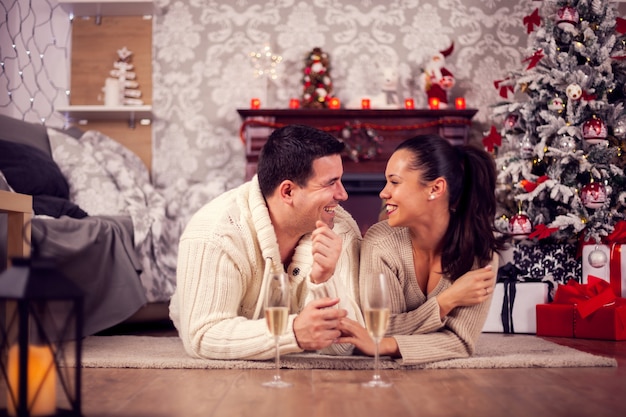 크리스마스 날 거실에 누워 있는 손을 잡고 있는 젊은 남편과 아내. 음료를 마시는 커플.