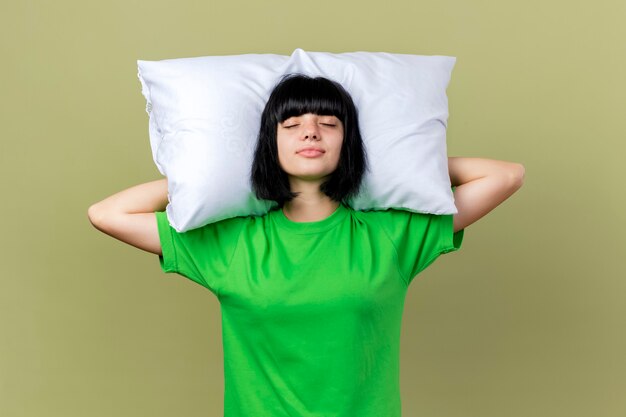 Young ill caucasian girl holding pillow under head with closed eyes isolated on olive green background