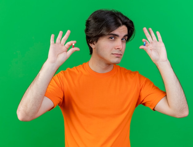 young ill man raising pills isolated on green