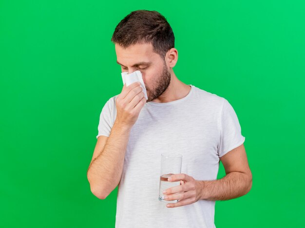 Young ill man wiping nose with napkin isolated on green background