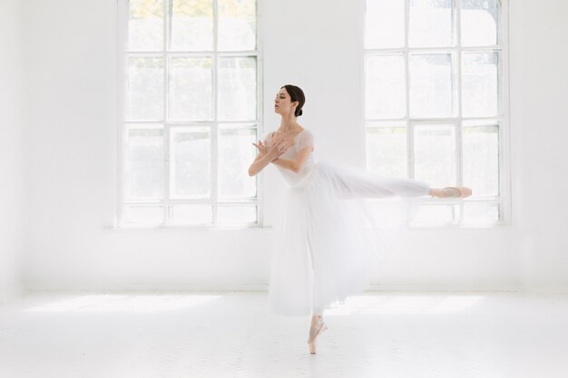 젊고 믿을 수 없을만큼 아름다운 발레리나는 흰색 스튜디오에서 포즈를 취하고 춤을 추고 있습니다.