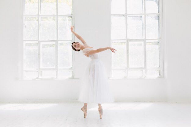 Молодая и невероятно красивая балерина позирует и танцует в белой студии