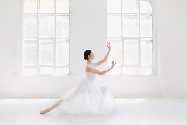 Young and incredibly beautiful ballerina is posing and dancing in a white studio