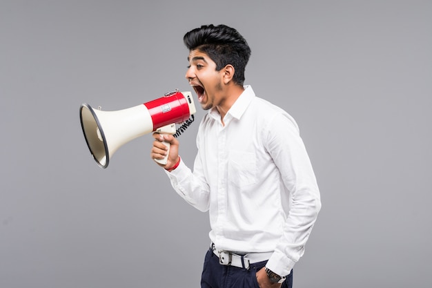 Young indian businessman announcing into a megaphone on gray wall