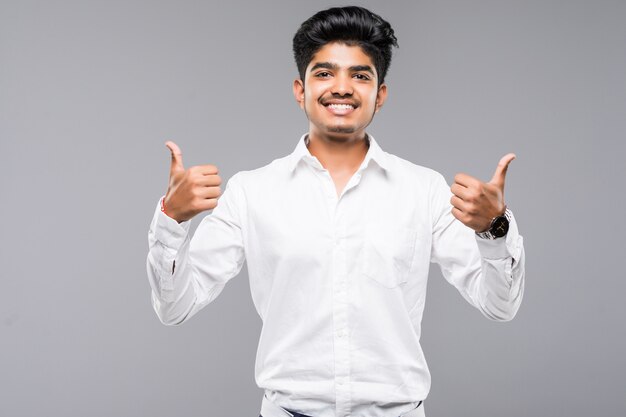 Young indian man standing over isolated grey wall approving doing positive gesture with hand, thumbs up smiling and happy for success