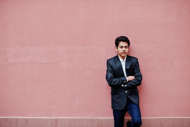 Young indian man on suit posed against pink wall