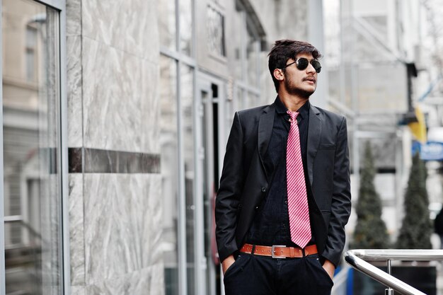 Молодой индийский мужчина в галстуке и солнцезащитных очках позирует на улице