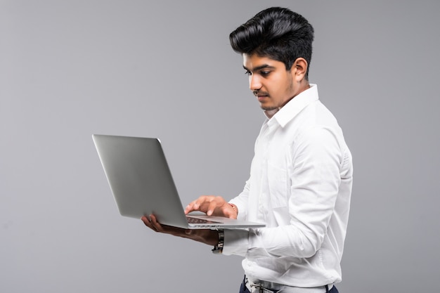 Young indian man with laptop on gray wall